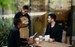 Imagen muestra a un hombre tomando la orden a dos amigos en un restaurante mientras ellos sostienen el menú. Hay dos cafés en la mesa.